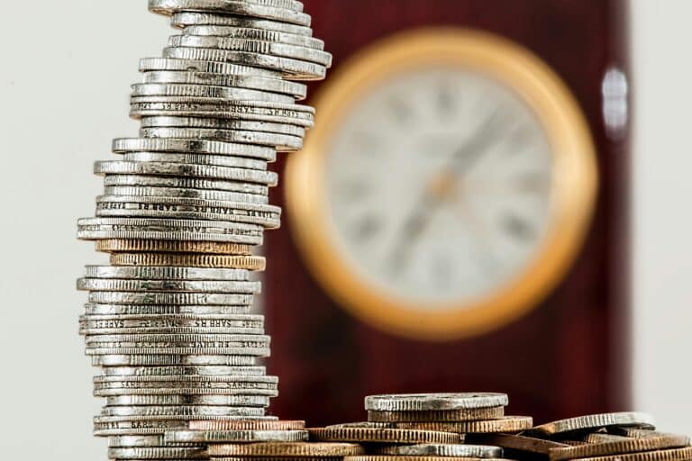 Une image en gros plan de pièces empilées avec une horloge floue, symbolisant la relation entre le temps et l'argent.